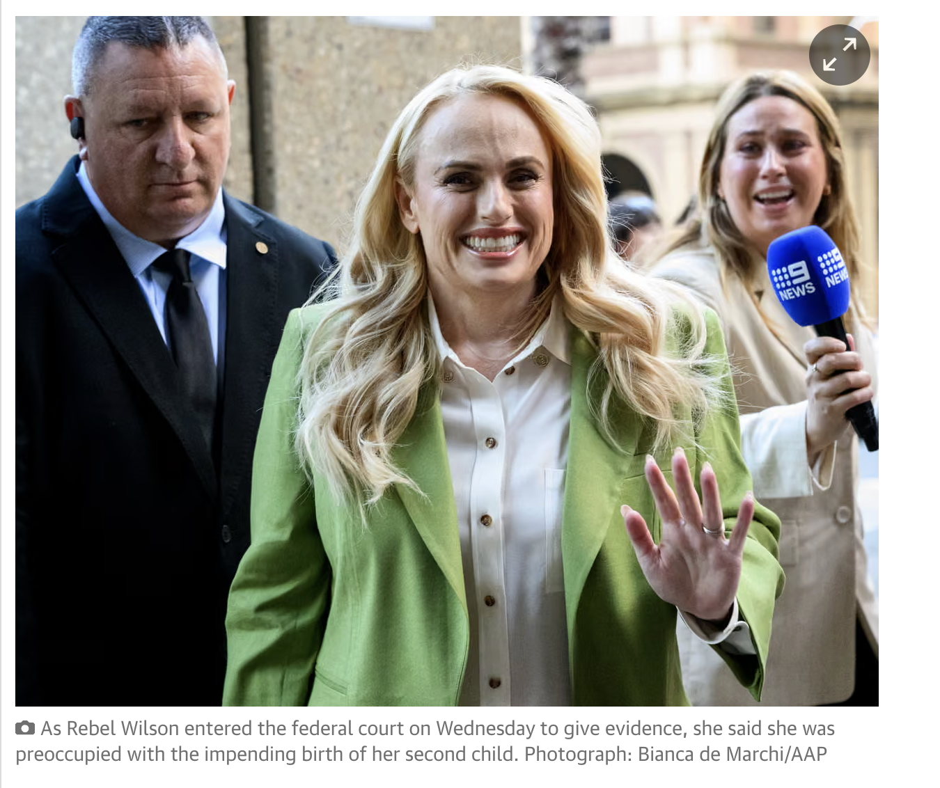 Rebel Wilson in a bright green blazer entering Federal Court of Australia, smiling and waving