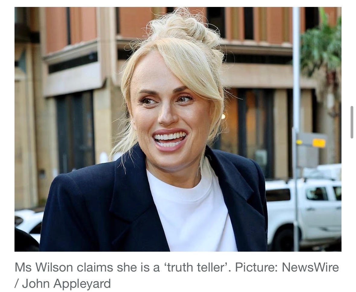 Rebel Wilson outside Federal Court of Australia, hair up, smiling, in navy blazer over white crew tee · Week 2 of MacInnes v. Wilson trial